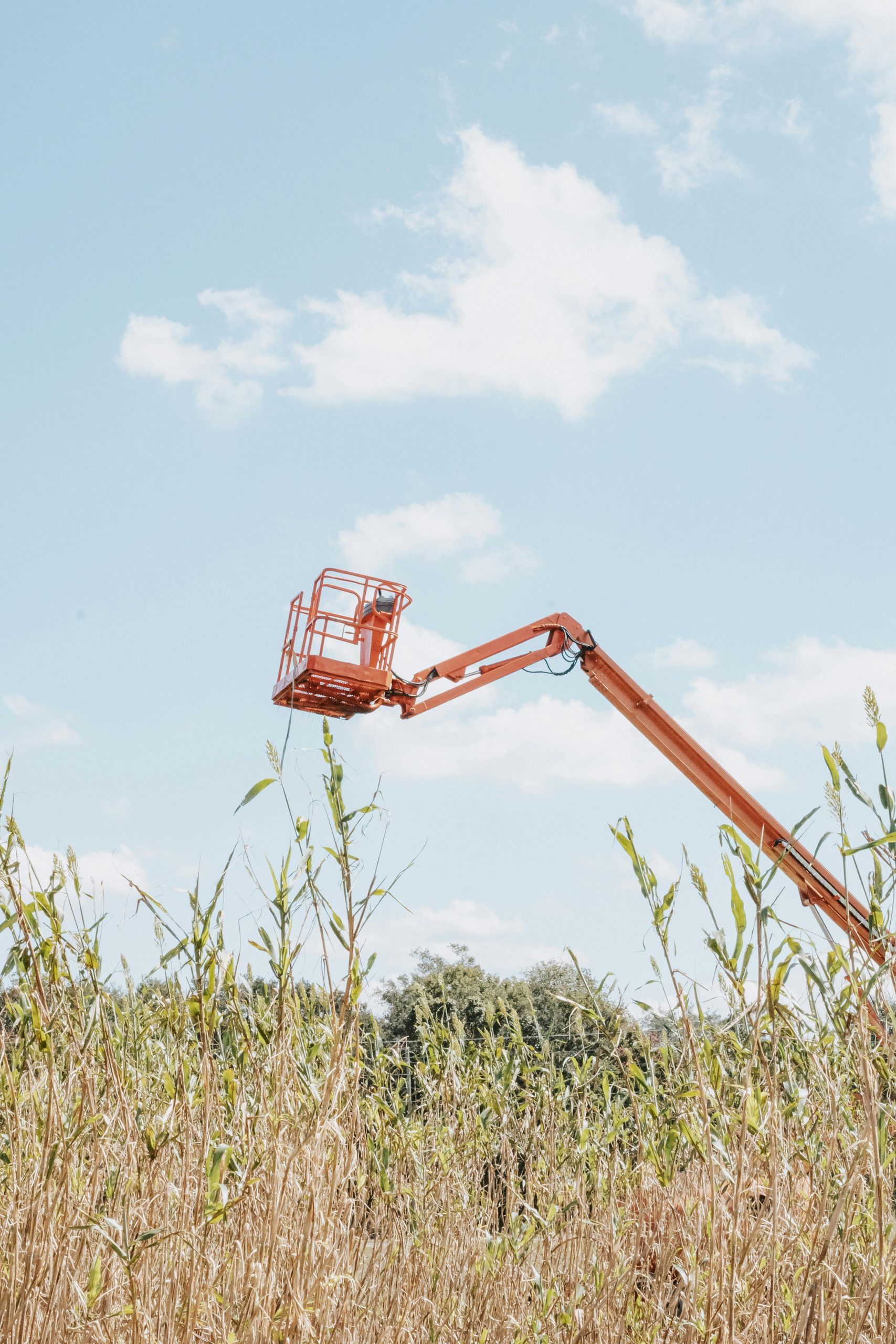 Orange boom lift elevating over a rural field with a clear blue sky.